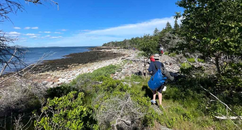 A person carries a duffle back toward a shore of a body of water. 